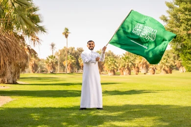 رجل سعودي يحمل العلم في حديقة خضراء رجل سعودي يحمل العلم في حديقة خضراء