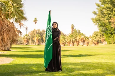 امرأة سعودية تحمل العلم السعودي في حديقة