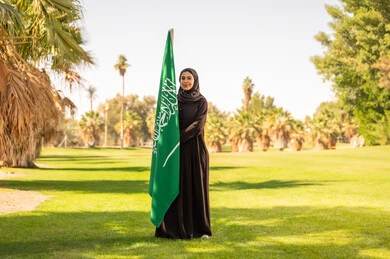 امرأة سعودية تحمل العلم الوطني في حديقة خضراء