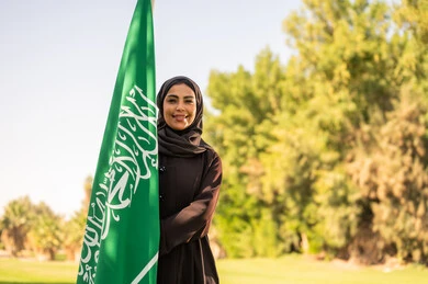 امرأة سعودية مبتسمة مع العلم الوطني في حديقة امرأة سعودية مبتسمة مع العلم الوطني في حديقة