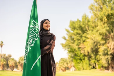 امرأة سعودية بالعباءة السوداء مع علم السعودية