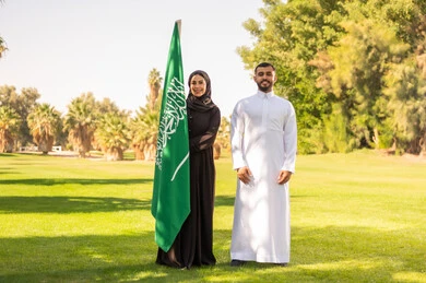 رجل وامرأة سعوديان يحملان العلم الوطني في حديقة