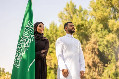 رجل وامرأة سعوديان مع علم المملكة في الخارج
