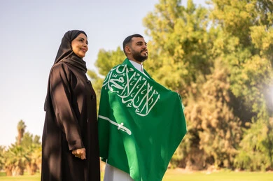 زوجان سعوديان مع العلم الوطني في حديقة خارجية