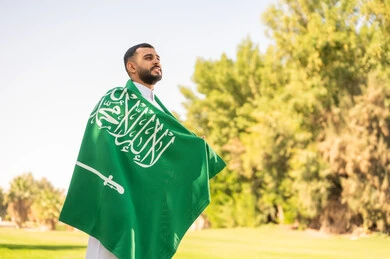 رجل سعودي يحمل العلم الوطني في حديقة عامة
