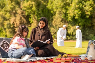 عائلة عُمانية في نزهة خارجية مع أم تقرأ لابنتها