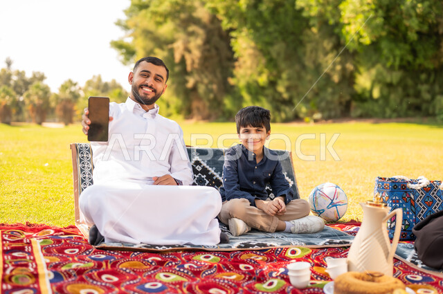 رجل سعودي وطفل مع هاتف ذكي في حديقة خارجية