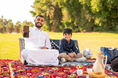 رجل سعودي وطفل مع هاتف ذكي في حديقة خارجية