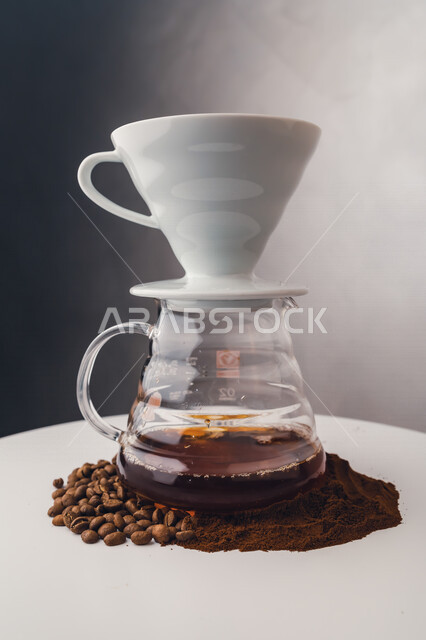 صورة لفنجان القهوة فوق وعاء القهوة الزجاجي الشفاف ، حبوب البن والقهوة المطحونة ، اعداد القهوة الخليجية ، مشروبات ساخنة 