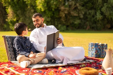 Saudi Father Reading Book to Son in Outdoor Park Saudi Father Reading Book to Son in Outdoor Park