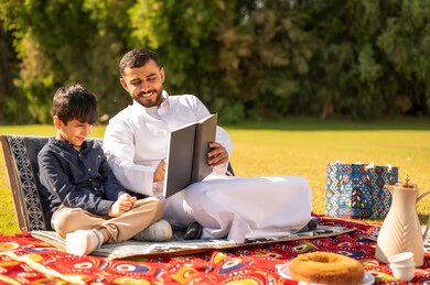 أب عربي يقرأ كتاباً لابنه في نزهة بالحديقة