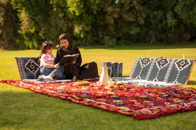 أم سعودية تقرأ كتاباً مع ابنتها في الحديقة