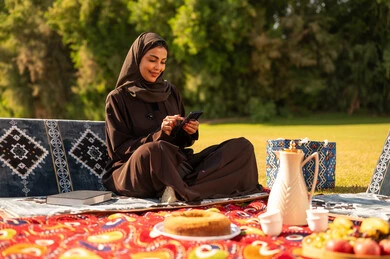 امرأة سعودية بالعباءة تستخدم الهاتف الذكي في نزهة خارجية