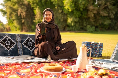 امرأة عربية بالعباءة تستخدم الهاتف في نزهة خارجية