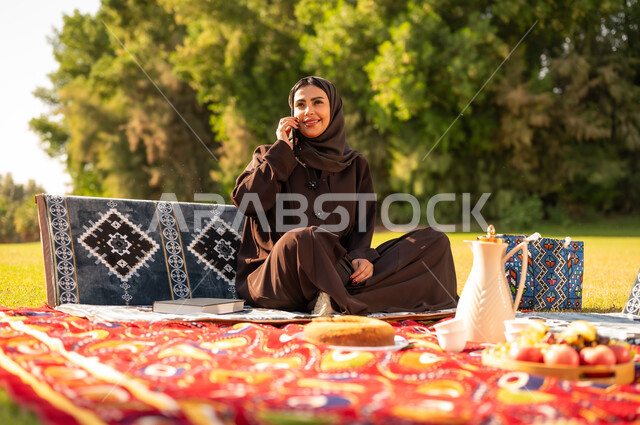 امرأة عربية بالعباءة تتحدث بالهاتف في الحديقة