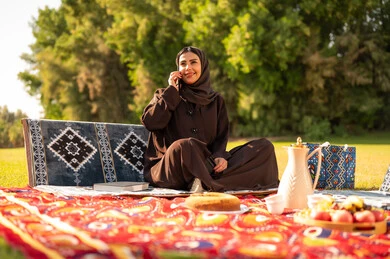 امرأة عربية بالعباءة تتحدث بالهاتف في الحديقة