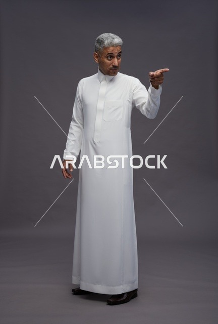 رجل سعودي بالثوب الأبيض يشير بإصبعه خلفية رمادية