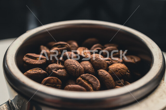 صورة مقربة لحبوب البن الداكنة في الذراع المعدني  ، اعداد كوب الاسبريسو ، صنع القهوة ، المشروبات الساخنة 