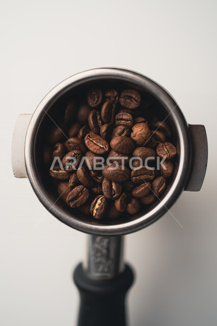 صورة مقربة لحبوب البن الداكنة في الذراع المعدني  ، اعداد كوب الاسبريسو ، صنع القهوة ، المشروبات الساخنة 