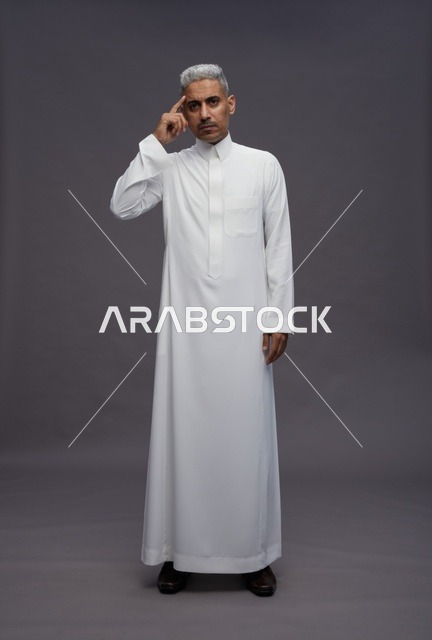 رجل سعودي بالثوب الأبيض يفكر أمام خلفية رمادية