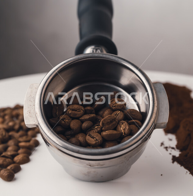 صورة مقربة لحبوب البن الداكنة في الذراع المعدني  ،  مجموعة من حبوب البن و القهوة المطحونة ، اعداد كوب الاسبريسو ، صنع القهوة ، المشروبات الساخنة 