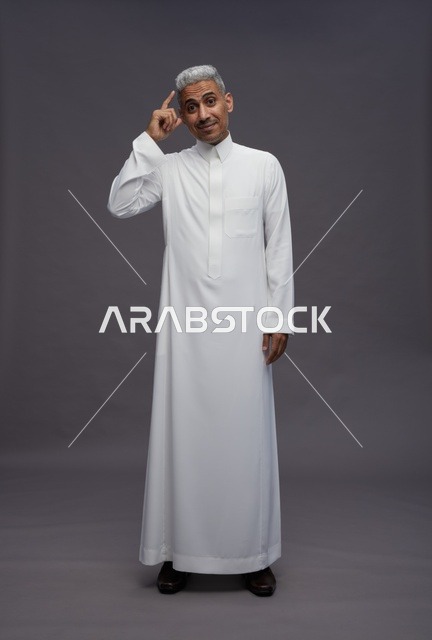 رجل سعودي بالثوب التقليدي يفكر خلف خلفية رمادية