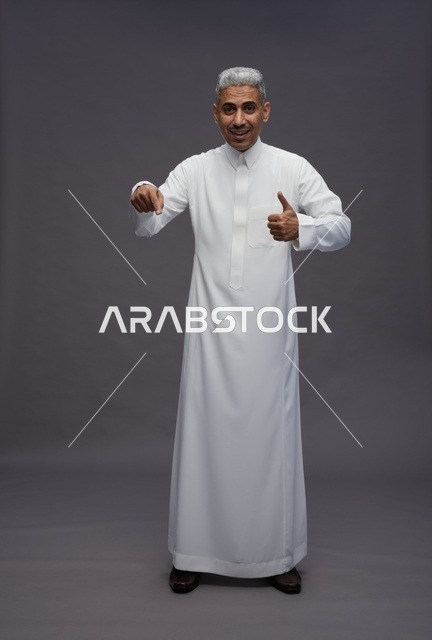 رجل سعودي بالثوب الأبيض يبتسم ويشير بالإبهام