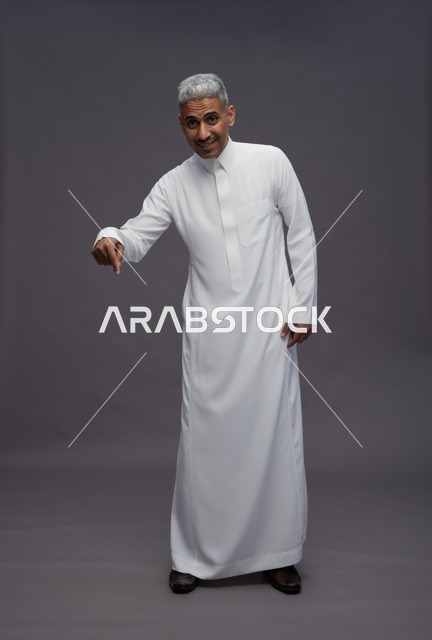 رجل سعودي يرتدي الثوب التقليدي الأبيض يشير للأسفل
