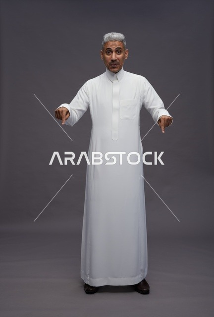 رجل سعودي بالثوب الأبيض يشير للأسفل خلفية رمادية