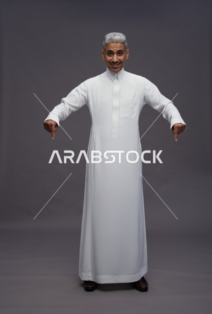 رجل سعودي بالثوب يشير للأسفل على خلفية رمادية