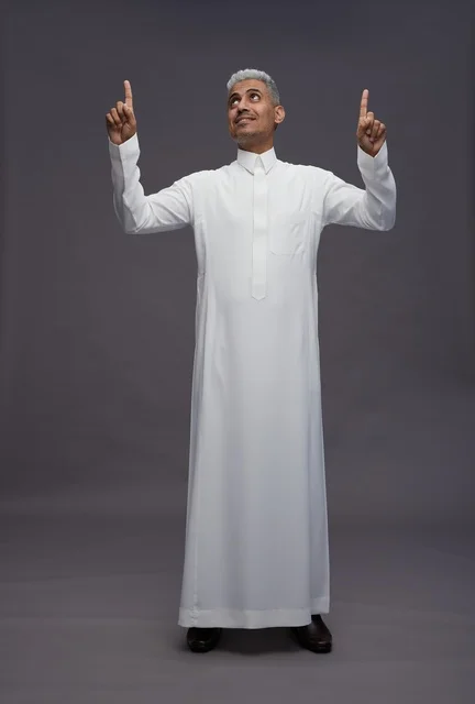 رجل سعودي بالثوب الأبيض يشير للأعلى خلفية رمادية
