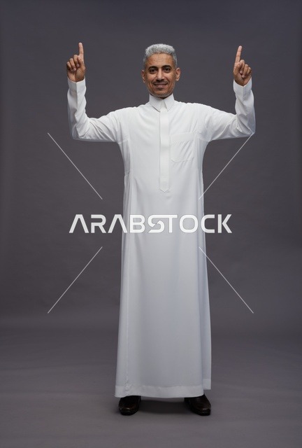 رجل سعودي بالثوب الأبيض يشير للأعلى خلفية رمادية
