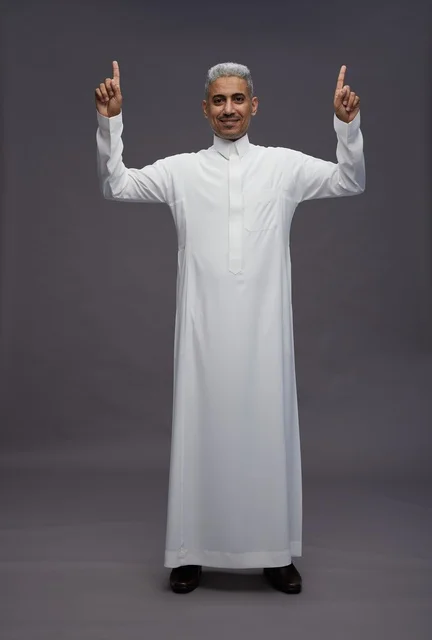 رجل سعودي بالثوب الأبيض يشير للأعلى خلفية رمادية