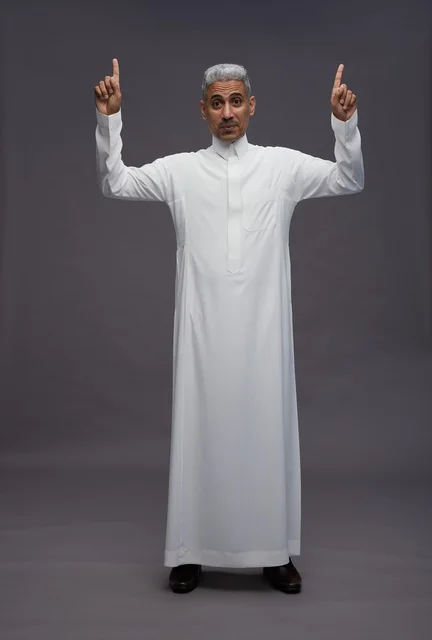 رجل سعودي بالثوب الأبيض يشير للأعلى بخلفية رمادية