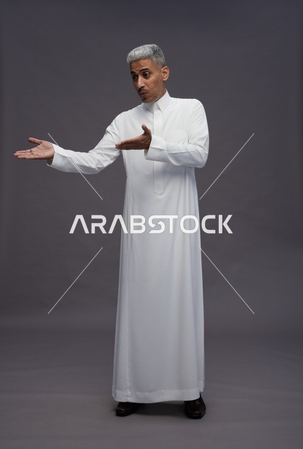 رجل سعودي بالثوب الأبيض يشير بيديه خلفية رمادية