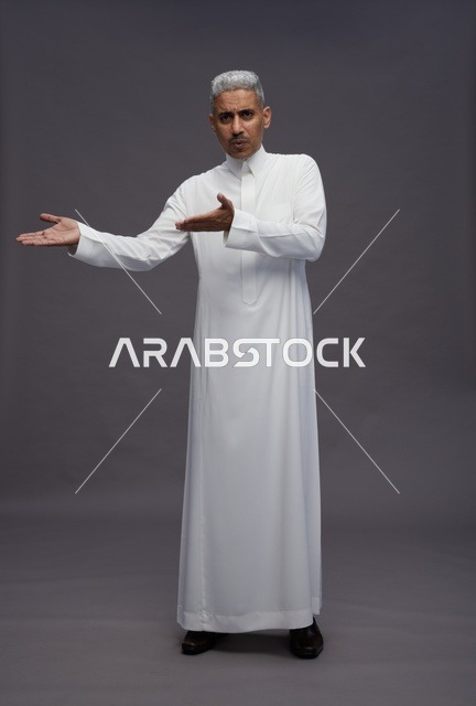 رجل سعودي بالثوب الأبيض يشير بيديه خلفية رمادية