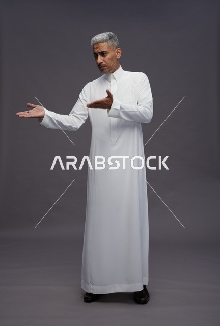 رجل سعودي بالثوب الأبيض يشير بيديه على خلفية رمادية