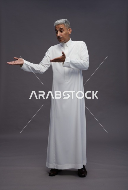 رجل سعودي بالثوب الأبيض يشير على خلفية رمادية