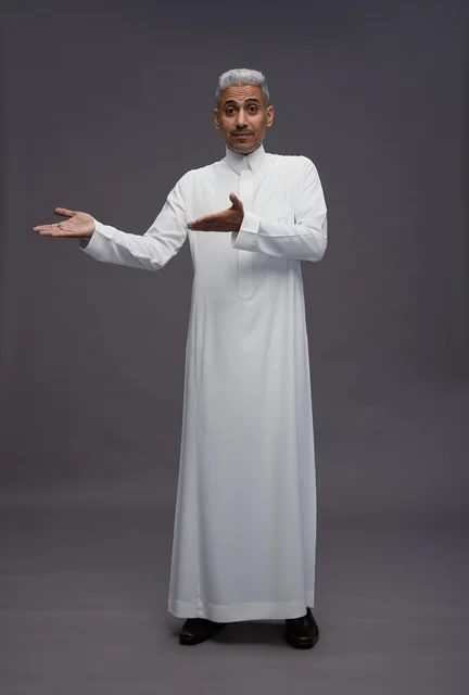 رجل سعودي بالثوب التقليدي يشير بيده أمام خلفية رمادية