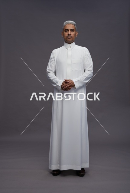 رجل سعودي بالثوب الأبيض التقليدي على خلفية رمادية