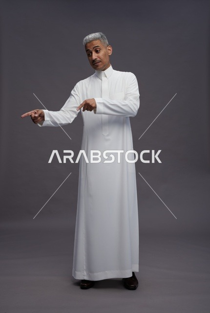 رجل سعودي بالثوب الأبيض يشير لليسار خلفية رمادية