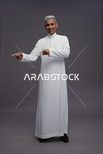 رجل سعودي بالثوب الأبيض يشير لليسار خلفية رمادية
