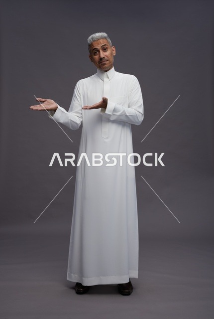 رجل سعودي بالثوب الأبيض يشير بيديه خلفية رمادية