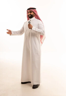 رجل سعودي يمسك ميكروفون مع إيماءة ترحيب