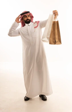 رجل سعودي مصدوم يحمل حقائب تسوق بخلفية بيضاء