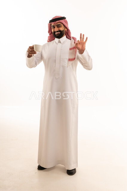 رجل سعودي بالثوب التقليدي يمسك فنجان قهوة في استوديو