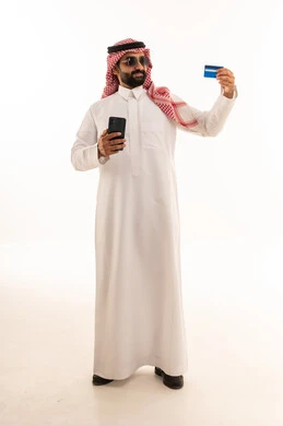 رجل سعودي يحمل هاتفاً وبطاقة بنكية بخلفية بيضاء