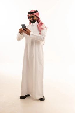 رجل سعودي بالثوب يستخدم الجوال على خلفية بيضاء