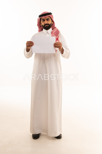 رجل سعودي يحمل ورقة بيضاء فارغة في الاستوديو