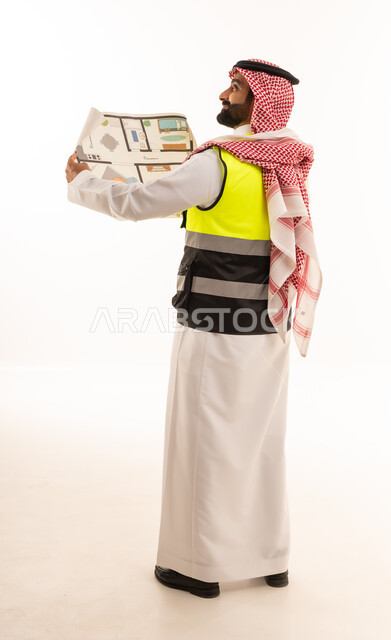 مهندس سعودي يرتدي سترة السلامة ويمسك مخطط بناء
